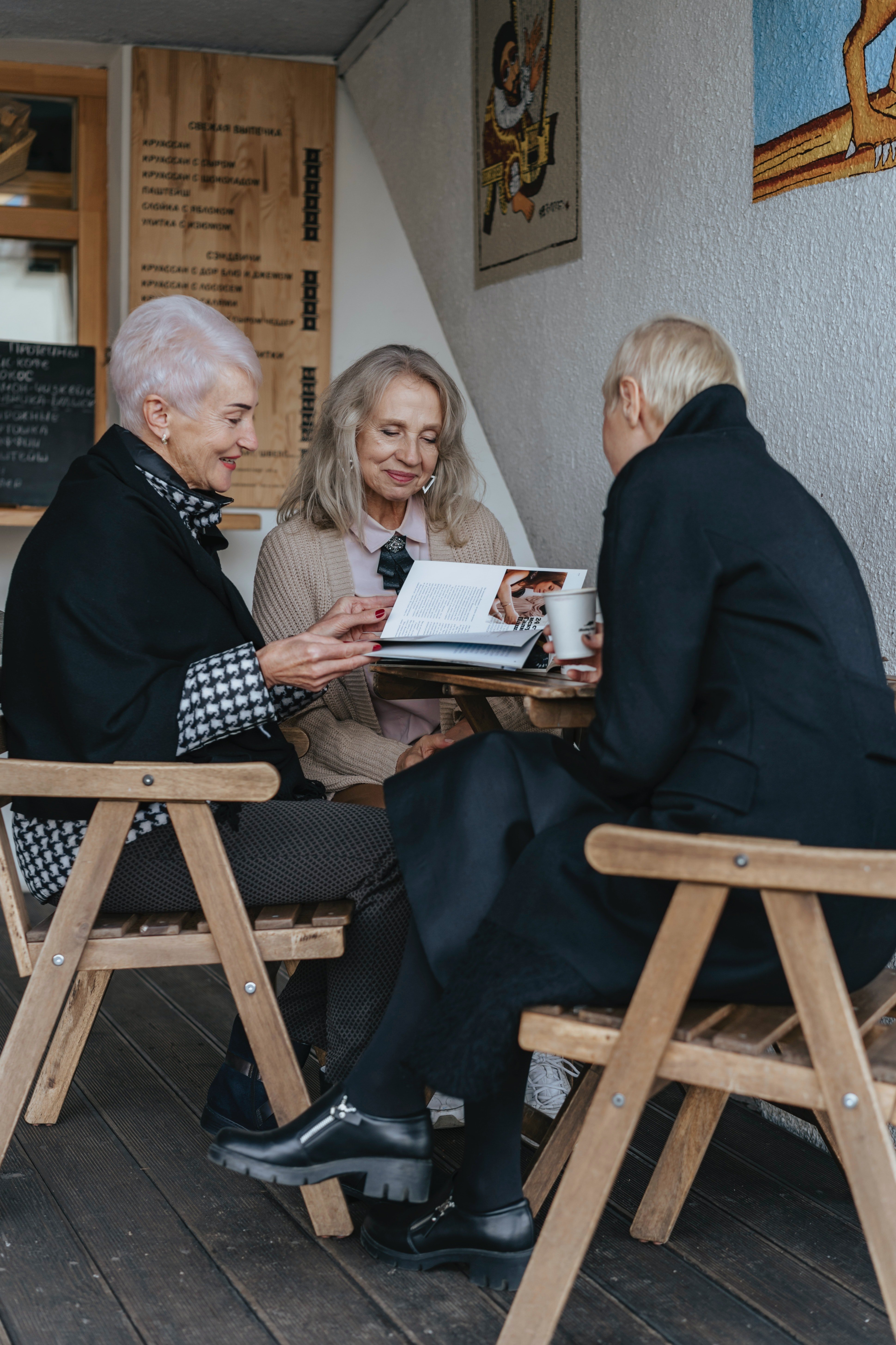 Three women sitting at a café table, reading a book together.